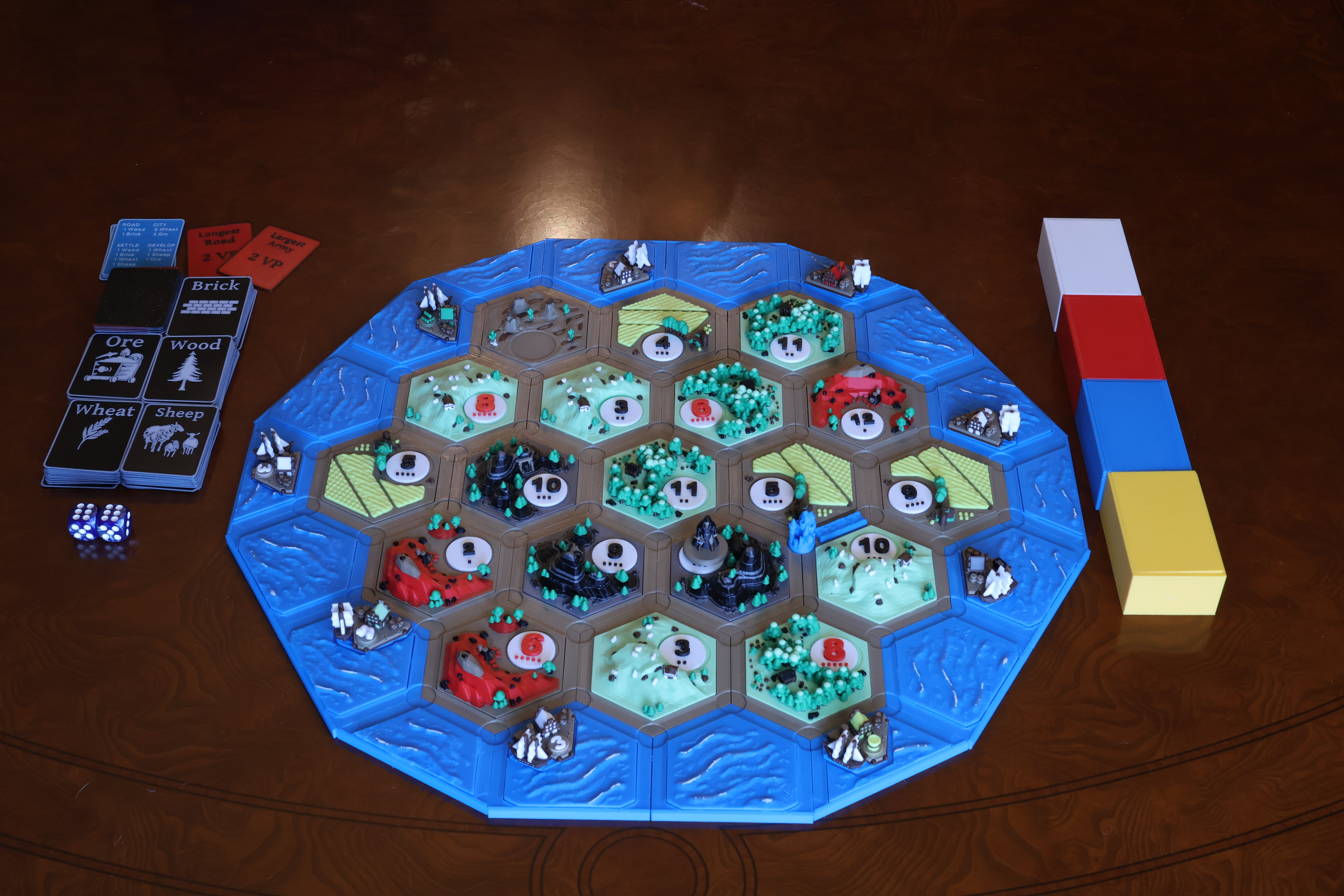 Full Catan Artisan set components laid out — magnetic hex tiles, settlements, cities, roads, custom robber, and number tokens